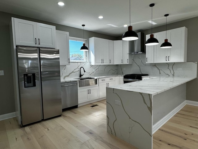 kitchen with wall chimney range hood, a peninsula, white cabinets, stainless steel appliances, and a sink