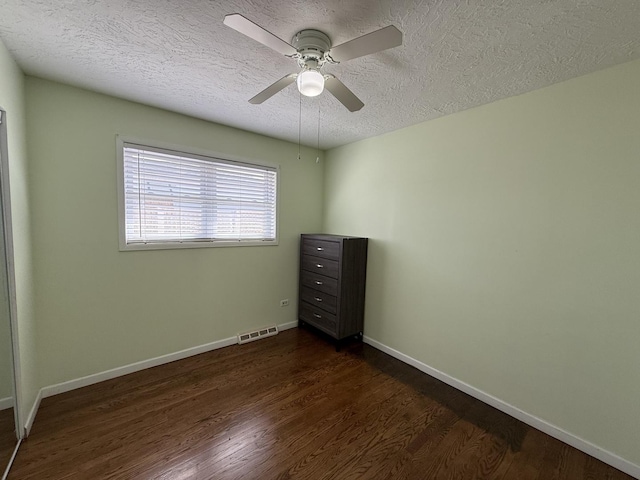 empty room with visible vents, a textured ceiling, dark wood-type flooring, and baseboards