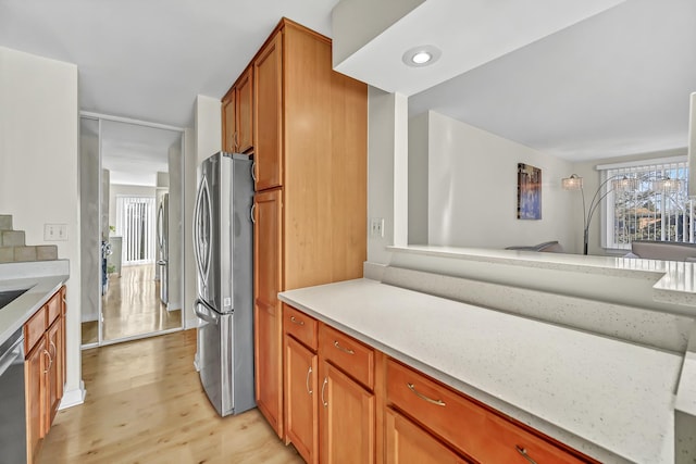 kitchen featuring stainless steel appliances, light wood-style floors, brown cabinetry, and light countertops