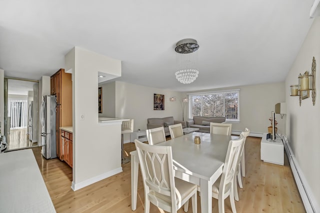 dining room with light wood finished floors, a chandelier, a baseboard heating unit, and baseboards