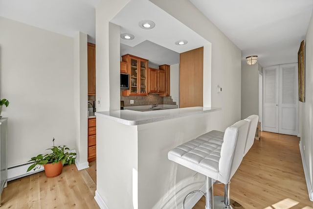 kitchen with brown cabinets, light wood-style flooring, tasteful backsplash, built in microwave, and glass insert cabinets