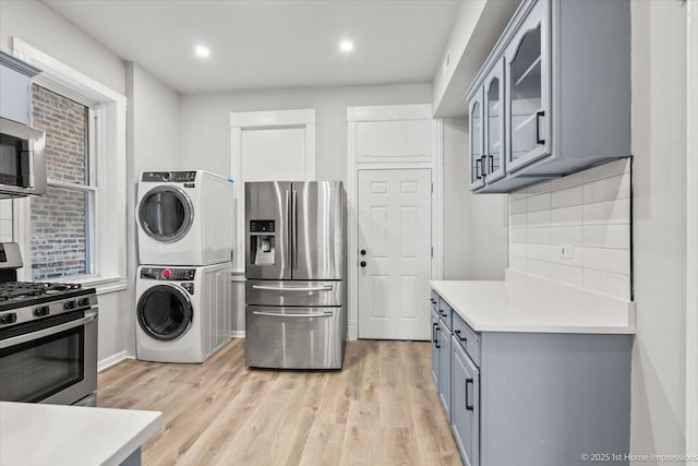 kitchen with light wood-type flooring, gray cabinets, stacked washer / drying machine, appliances with stainless steel finishes, and tasteful backsplash