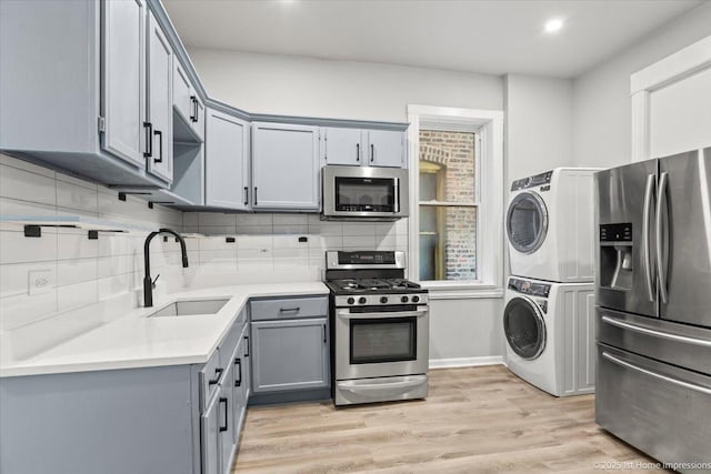 kitchen with backsplash, gray cabinets, appliances with stainless steel finishes, stacked washing maching and dryer, and a sink