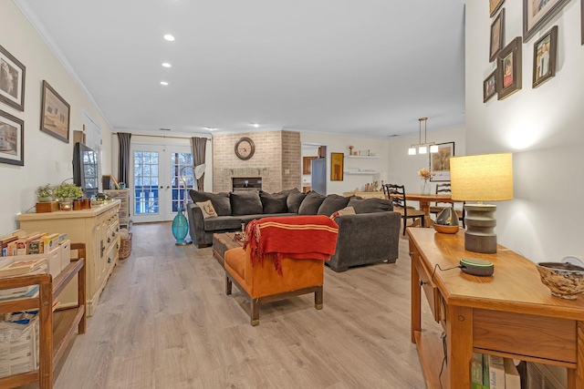 living room with light wood-type flooring, french doors, a brick fireplace, and crown molding