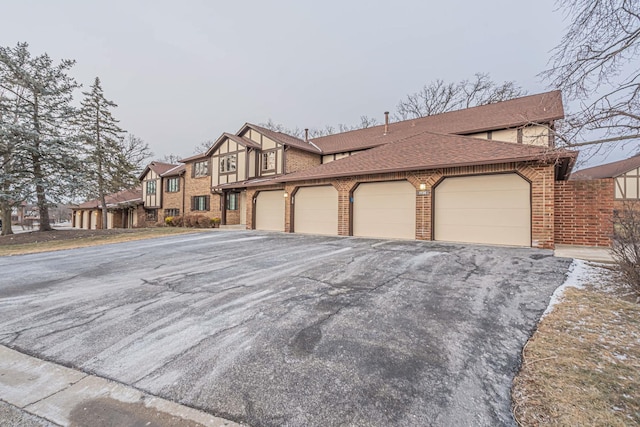 view of front of property with a garage, brick siding, driveway, and roof with shingles