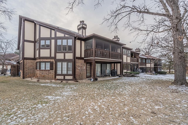 snow covered rear of property with stucco siding, brick siding, a sunroom, and a chimney