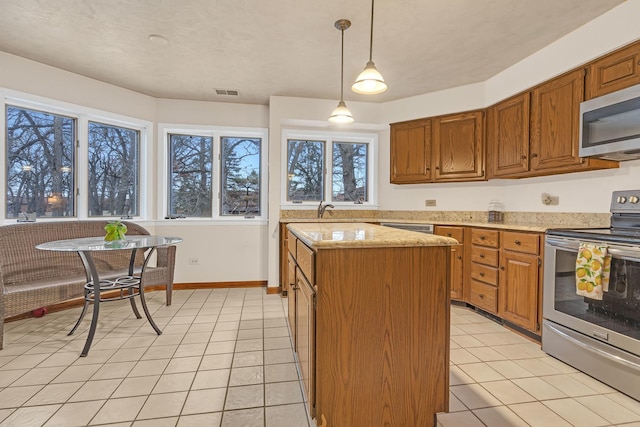 kitchen featuring visible vents, a center island, pendant lighting, brown cabinetry, and stainless steel appliances