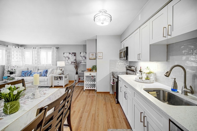 kitchen featuring light wood-type flooring, light stone counters, appliances with stainless steel finishes, white cabinetry, and a sink