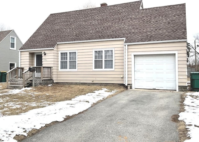 cape cod-style house with an attached garage, a chimney, driveway, and a shingled roof