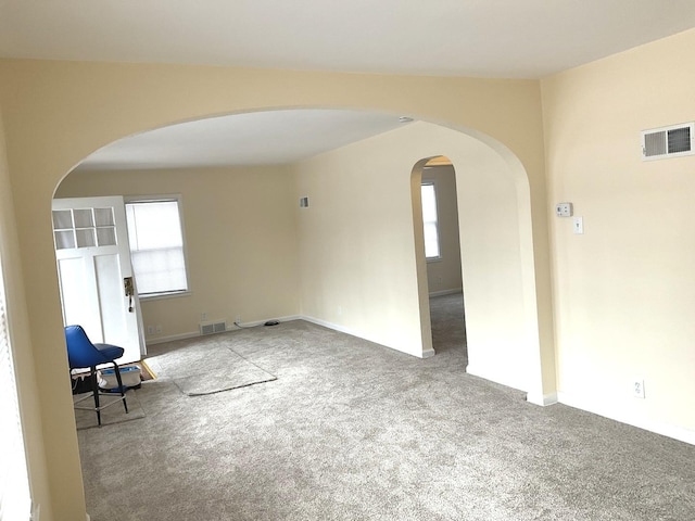 carpeted spare room with visible vents and arched walkways