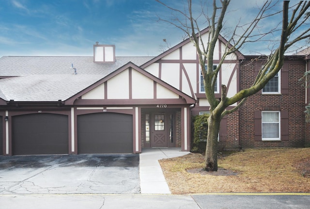 english style home featuring driveway, roof with shingles, stucco siding, a garage, and brick siding