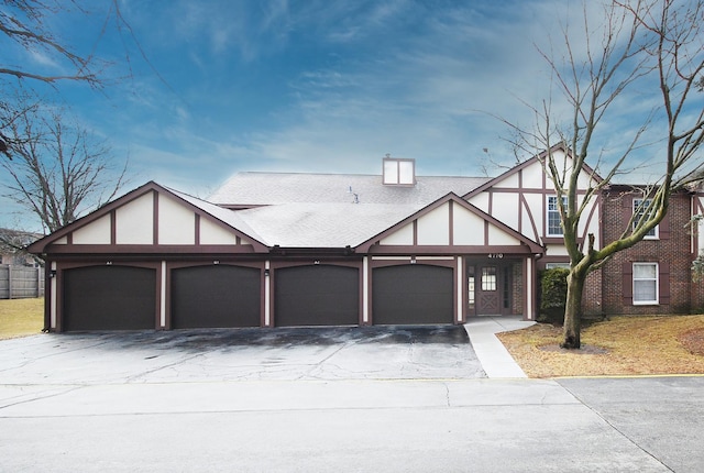 tudor-style house featuring stucco siding, an attached garage, driveway, and roof with shingles