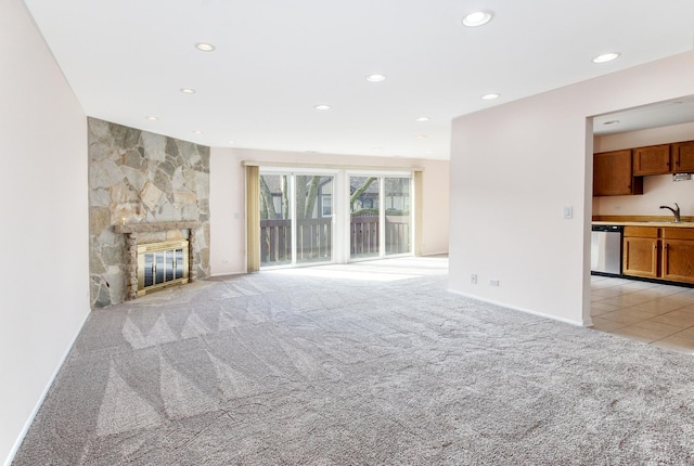 unfurnished living room with light tile patterned flooring, recessed lighting, a sink, a stone fireplace, and light carpet