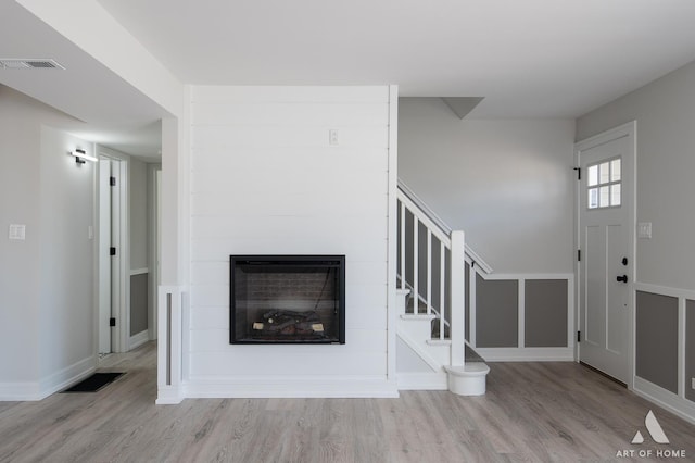 unfurnished living room featuring visible vents, a fireplace, stairs, and wood finished floors