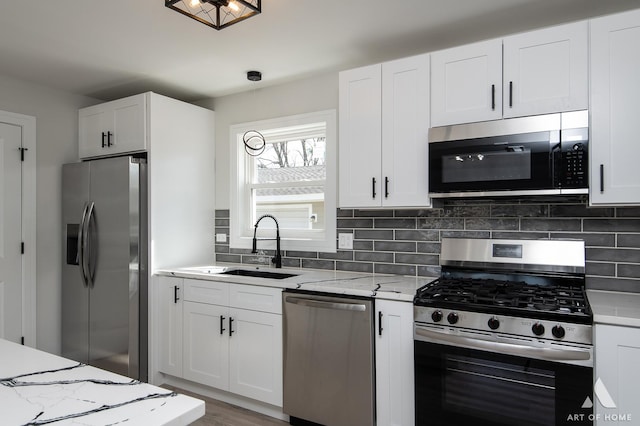 kitchen with backsplash, light stone counters, white cabinets, stainless steel appliances, and a sink