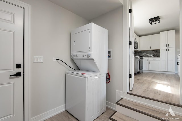 laundry area featuring laundry area, baseboards, stacked washer and clothes dryer, and light wood-type flooring