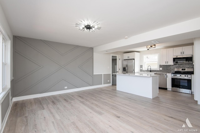 kitchen with a sink, light wood-style floors, appliances with stainless steel finishes, light countertops, and decorative backsplash