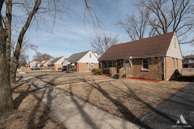 view of front of home with a residential view, brick siding, and a shingled roof