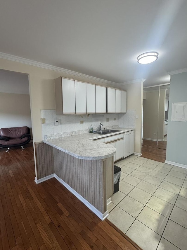 kitchen with crown molding, light countertops, decorative backsplash, a peninsula, and a sink