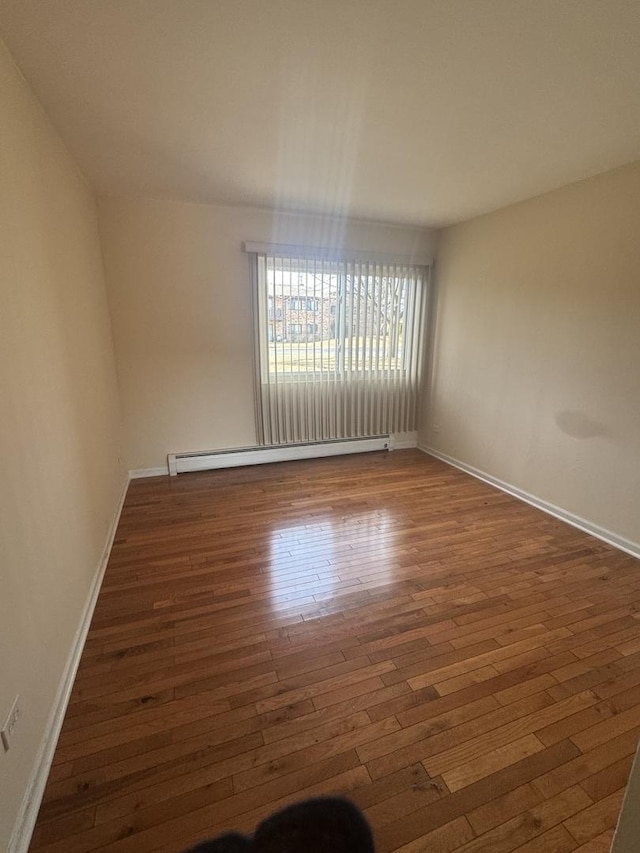 empty room with hardwood / wood-style floors, baseboards, and a baseboard radiator