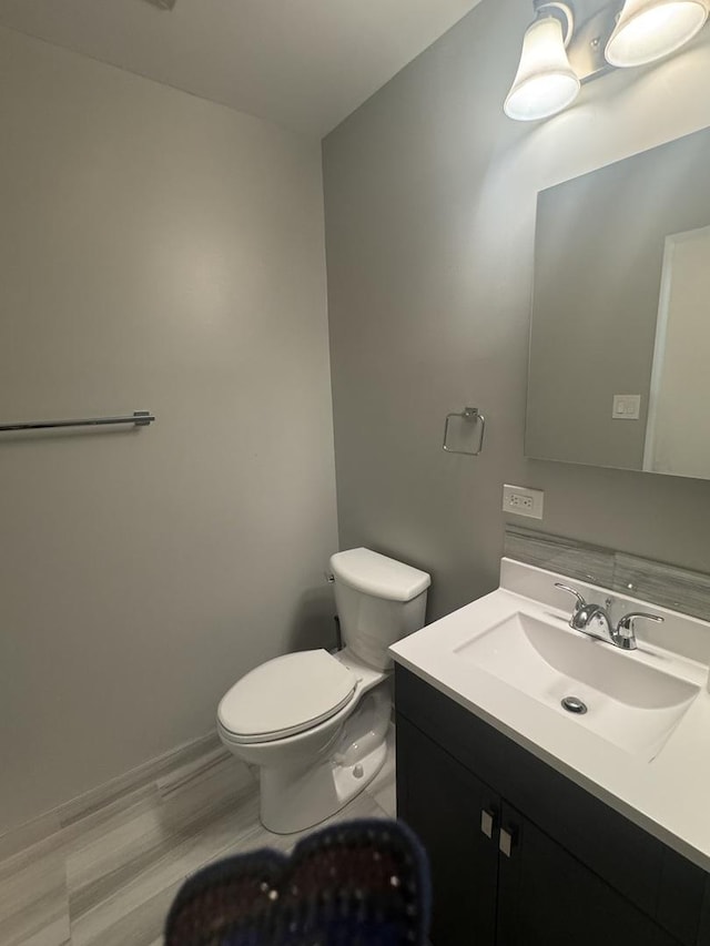 half bath featuring vanity, toilet, wood finished floors, and baseboards