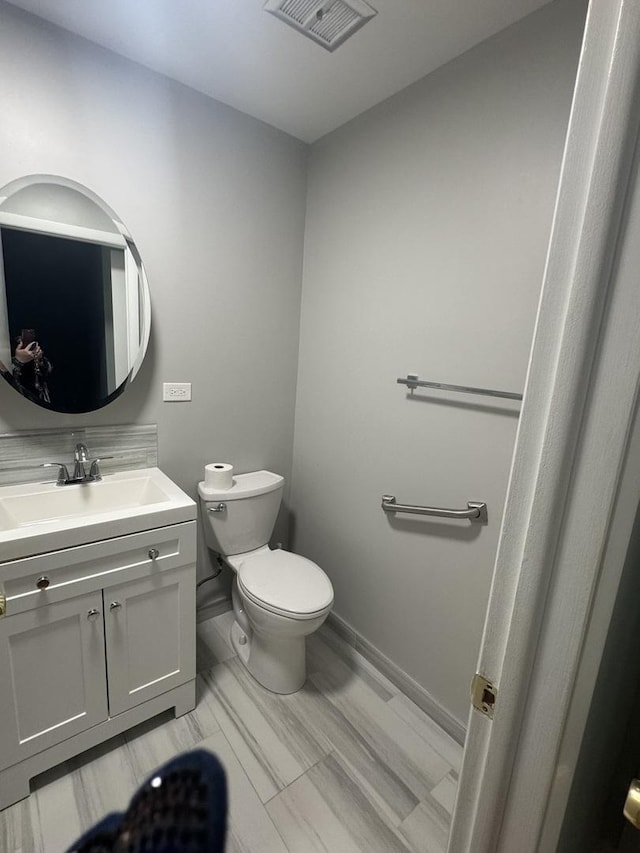 half bath featuring visible vents, toilet, vanity, and baseboards