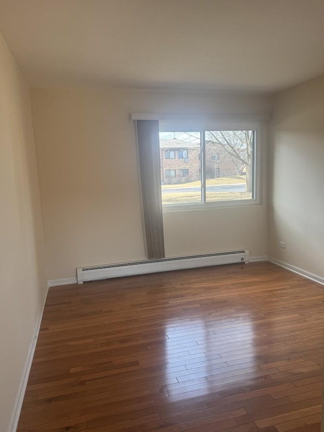 spare room featuring a baseboard heating unit, baseboards, and wood finished floors