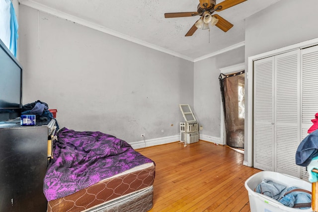 bedroom featuring a ceiling fan, hardwood / wood-style floors, a closet, crown molding, and baseboards