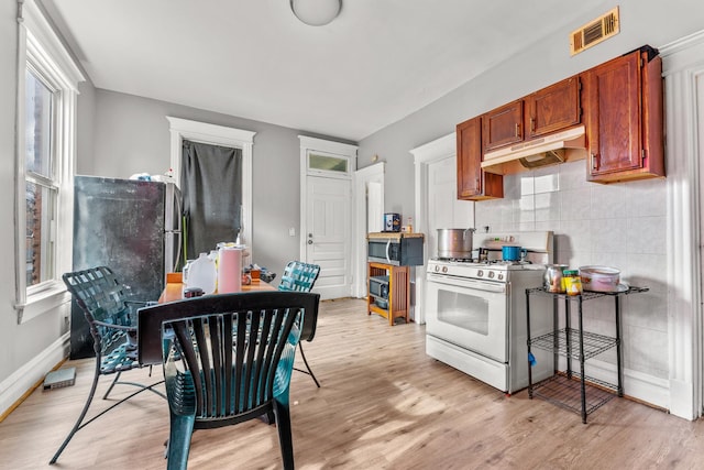 kitchen featuring visible vents, under cabinet range hood, backsplash, light wood finished floors, and white gas range