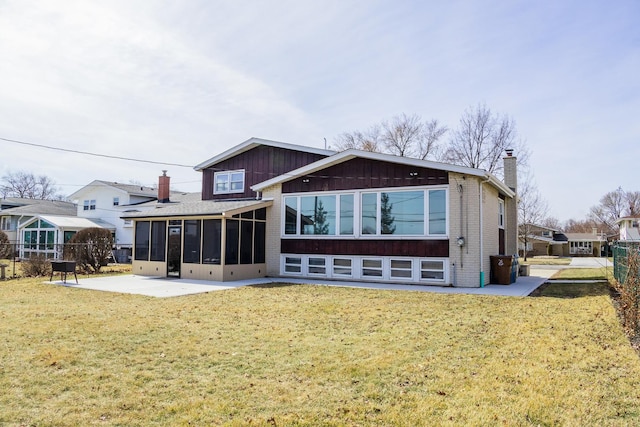 back of property featuring a yard, brick siding, a sunroom, and a chimney