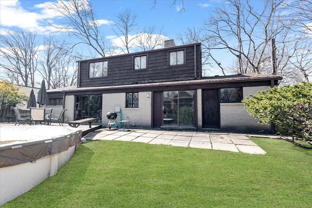 rear view of property featuring brick siding, a patio area, a lawn, and a chimney