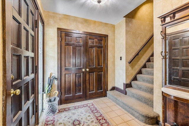 foyer featuring light tile patterned flooring, stairs, and baseboards