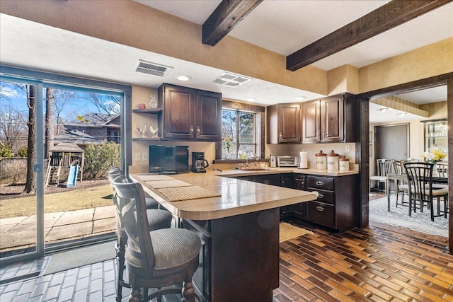 kitchen featuring visible vents, light countertops, a peninsula, brick floor, and a sink