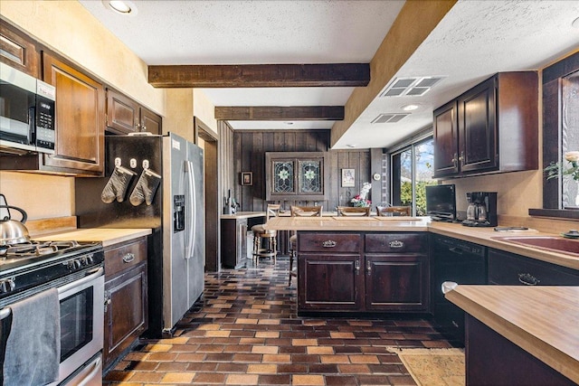 kitchen featuring brick floor, visible vents, appliances with stainless steel finishes, and beamed ceiling