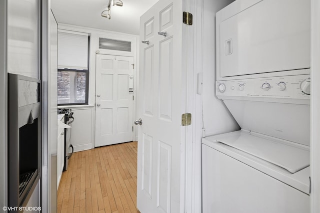 laundry area with laundry area, light wood-style flooring, and stacked washer / drying machine