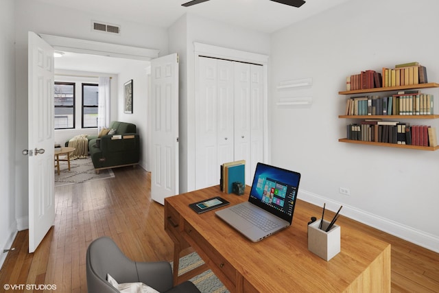 office area with visible vents, wood-type flooring, baseboards, and ceiling fan