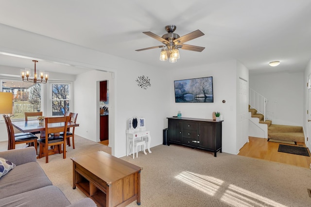 living room with light carpet, stairway, and ceiling fan with notable chandelier