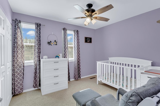 bedroom featuring a nursery area, a ceiling fan, and baseboards