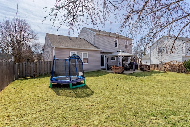 rear view of house with a trampoline, a gazebo, a fenced backyard, a yard, and a patio