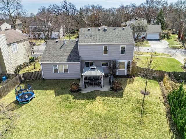 rear view of house featuring a trampoline, roof with shingles, a lawn, a fenced backyard, and a patio