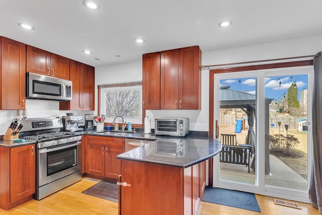 kitchen featuring dark stone countertops, appliances with stainless steel finishes, a peninsula, light wood-style floors, and a sink