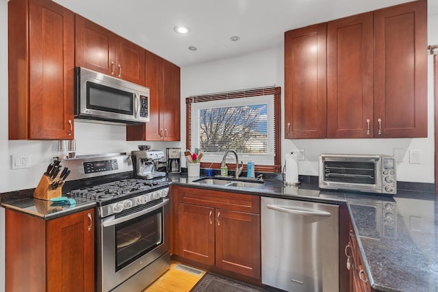 kitchen with a sink, dark stone counters, appliances with stainless steel finishes, and a toaster