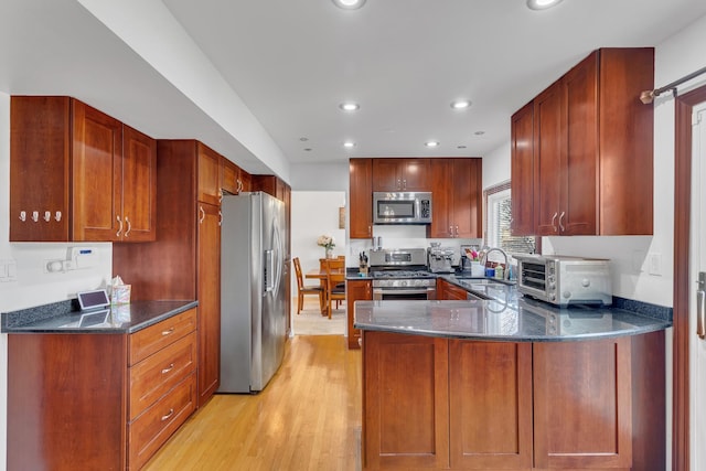 kitchen featuring dark stone counters, recessed lighting, a sink, stainless steel appliances, and light wood-type flooring