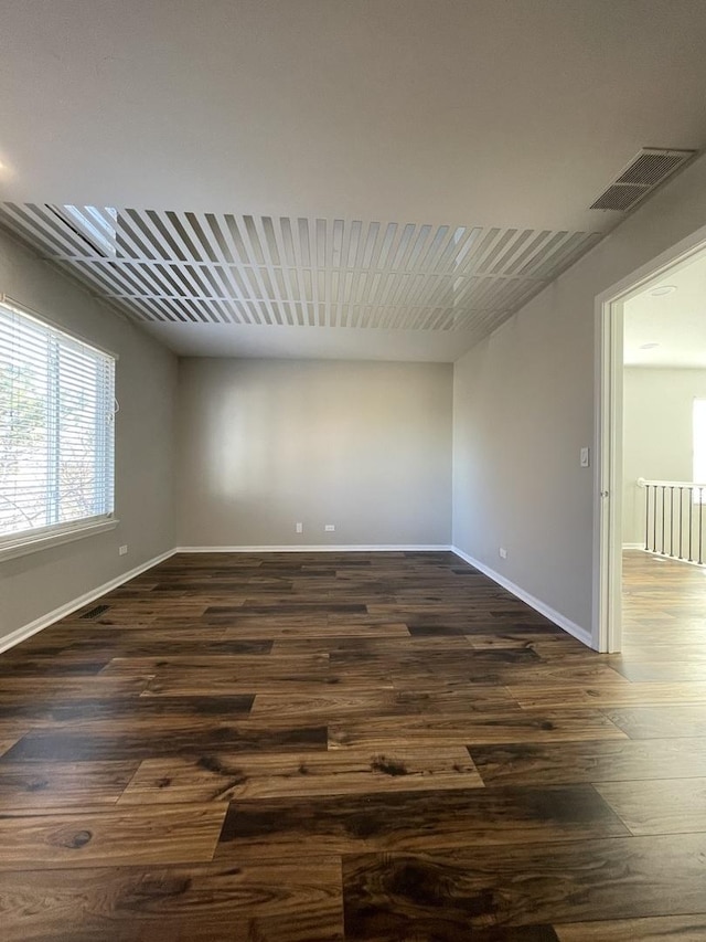 empty room with dark wood finished floors, baseboards, and visible vents