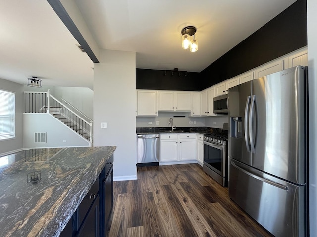 kitchen featuring visible vents, dark wood finished floors, dark stone counters, appliances with stainless steel finishes, and white cabinetry