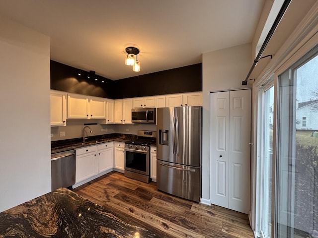 kitchen with a sink, dark countertops, dark wood finished floors, stainless steel appliances, and white cabinets