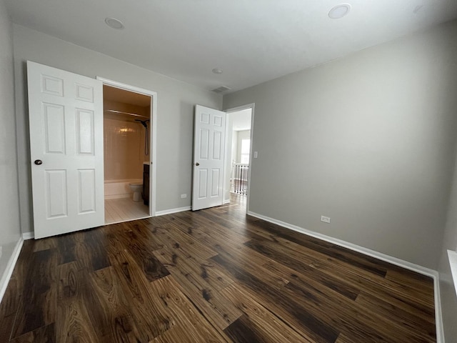 unfurnished bedroom featuring dark wood-style floors, baseboards, and connected bathroom