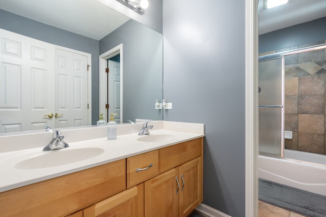 bathroom featuring double vanity, baseboards, combined bath / shower with glass door, and a sink