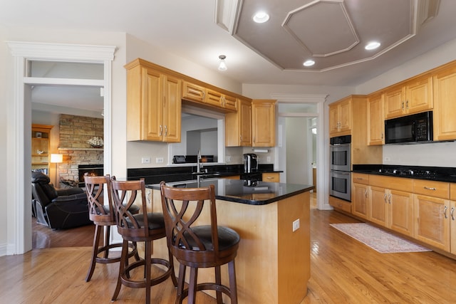 kitchen with light wood-type flooring, black appliances, a kitchen breakfast bar, dark countertops, and a fireplace