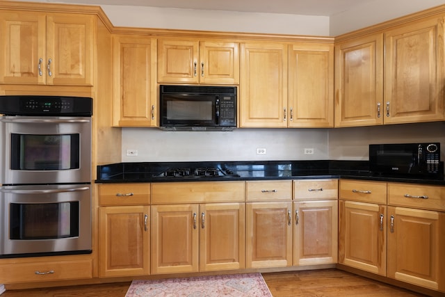 kitchen featuring black appliances, light wood-style flooring, and dark stone countertops